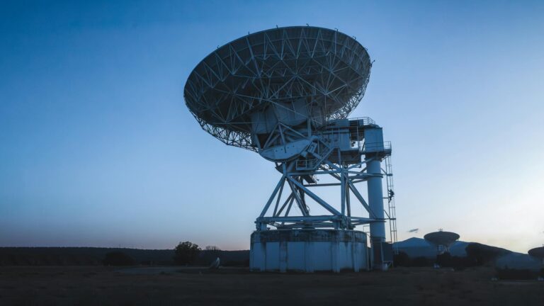 A large radio telescope under a clear evening sky captures cosmic signals.