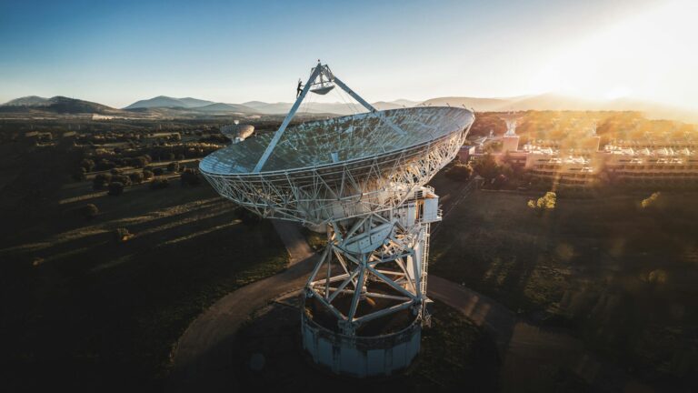 Aerial shot of a large satellite dish in a rural landscape during sunrise, showcasing technology and nature.