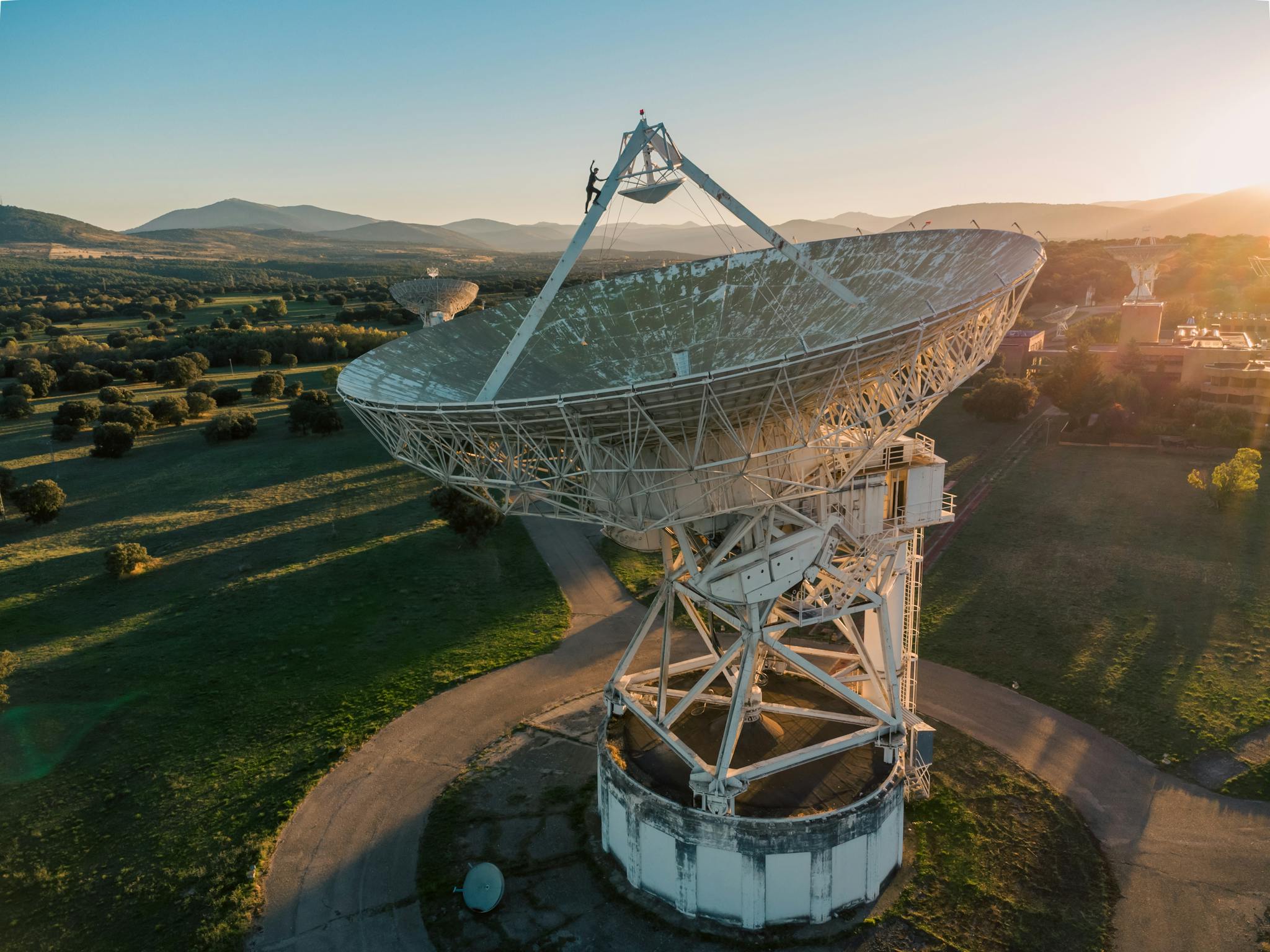 Aerial shot of a large satellite dish in a lush landscape at sunrise.